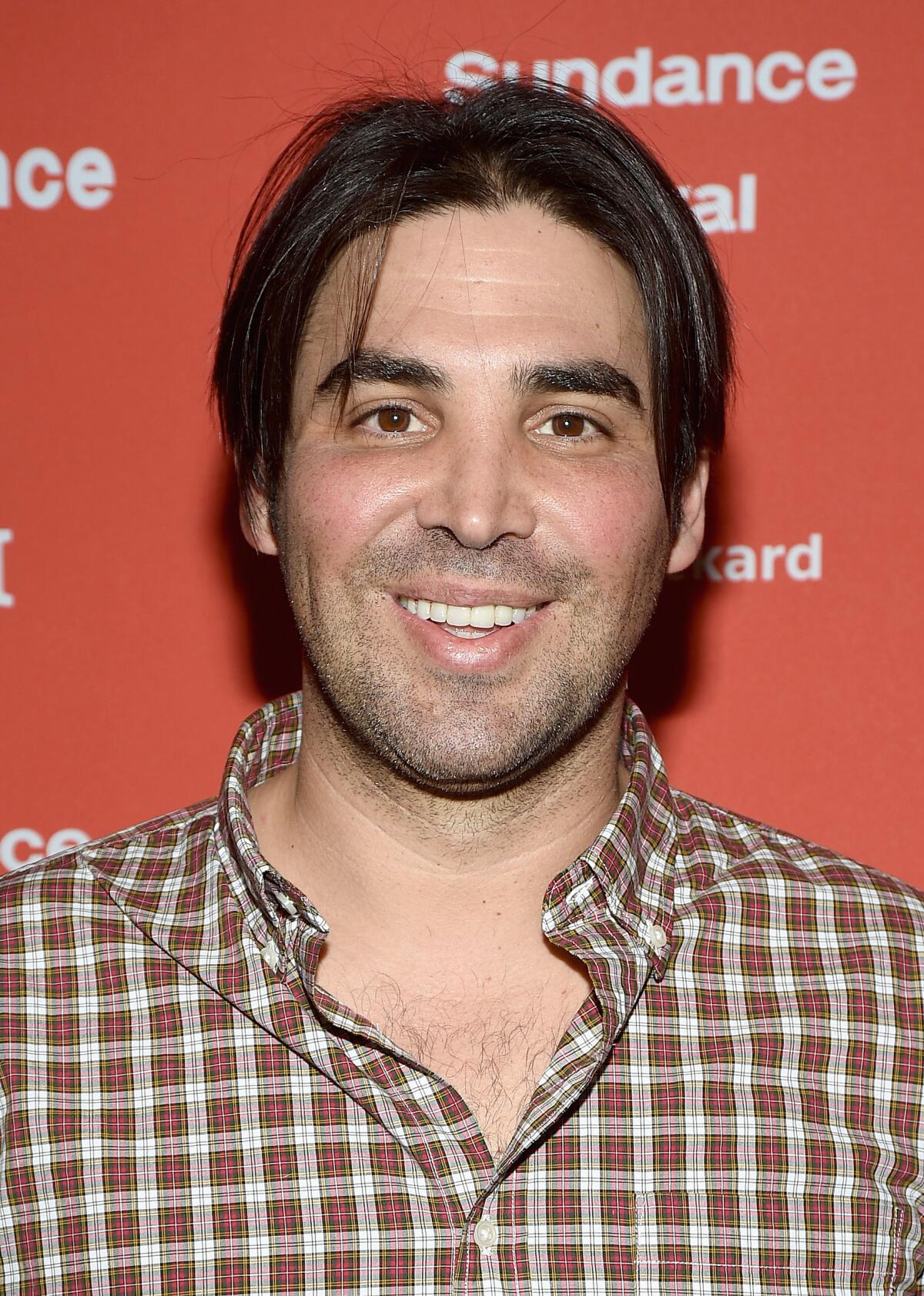 A man with dark hair and facial stubble smiles.