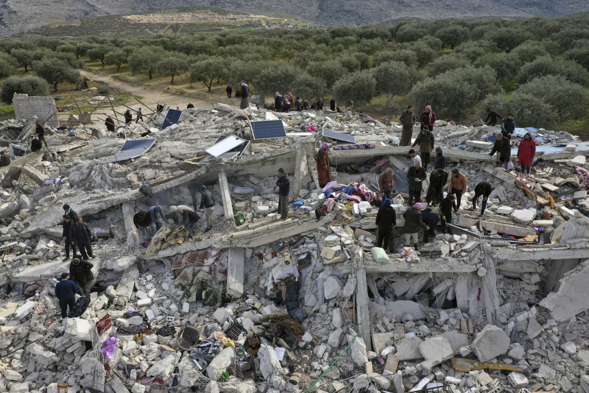 People stand atop a pile of collapsed buildings as they search through the rubble.