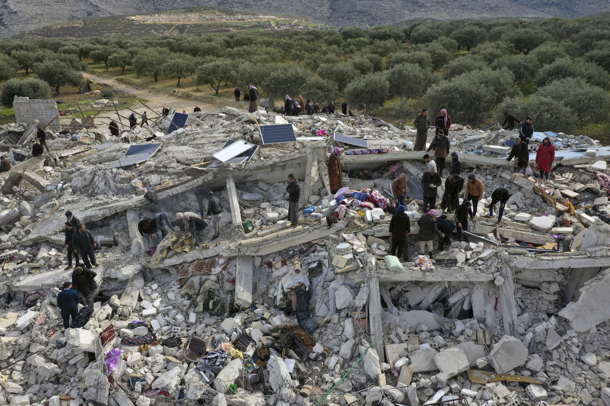 People stand atop a pile of collapsed buildings as they search through the rubble.