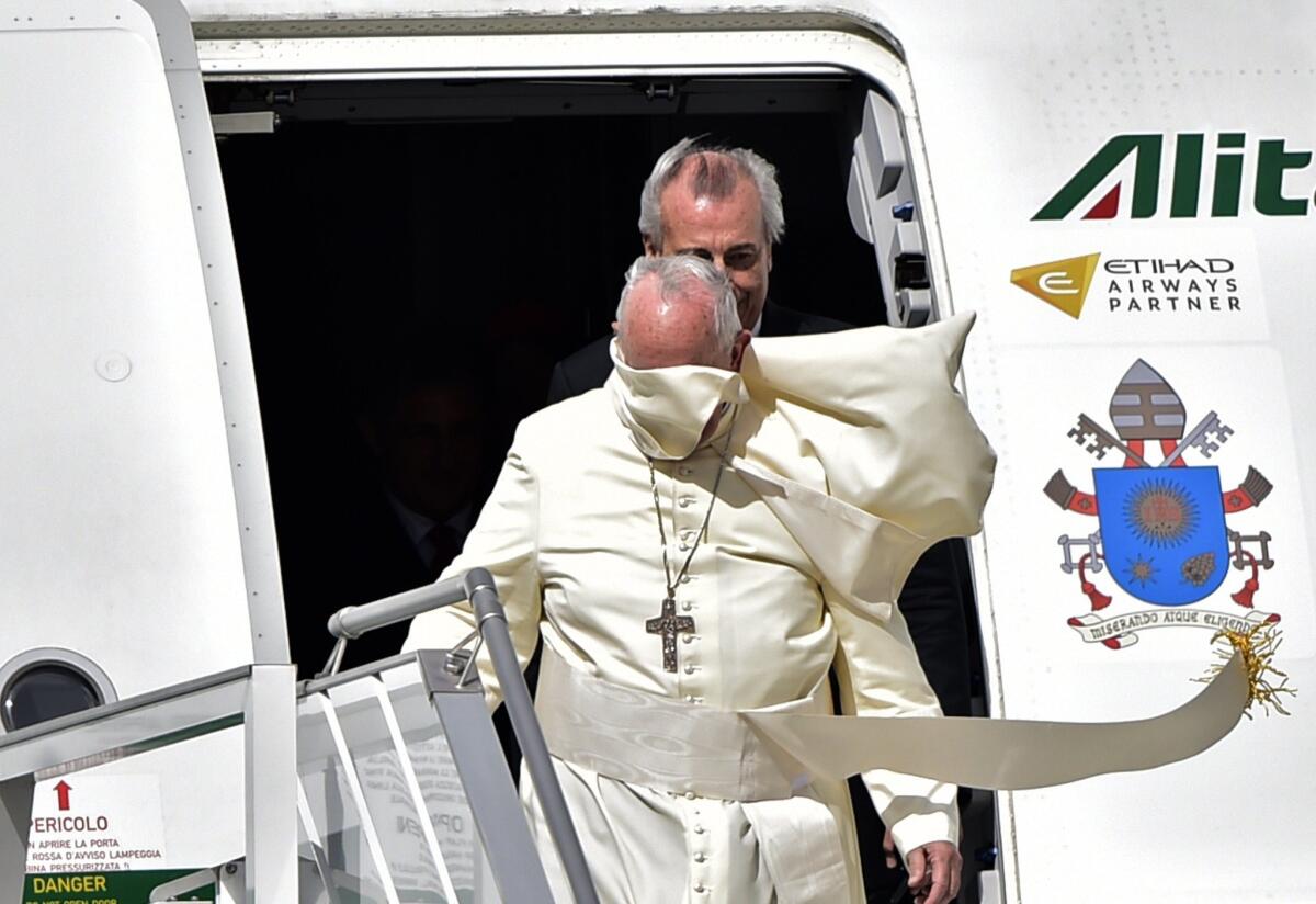As wind whips his garments, Pope Francis alights from an airplane upon landing at the Mariscal Sucre International Airport in Quito, Ecuador, on Sunday.