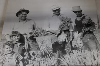 An old photograph of men in hats, holding flowers, with two young children