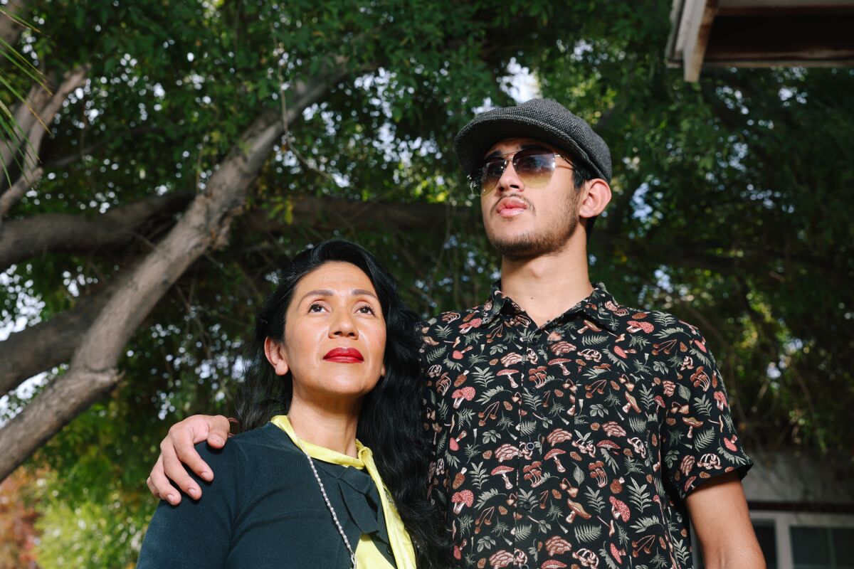 A mother and son pose together outside their home.