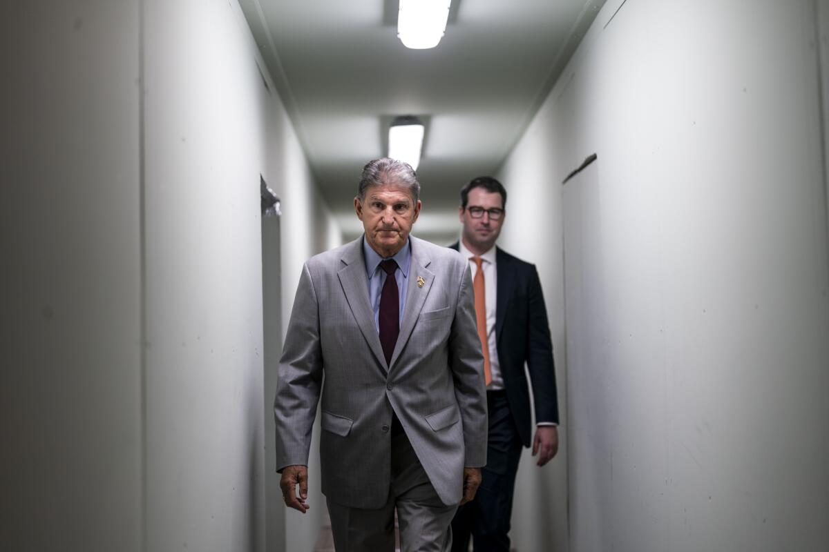 Sen. Joe Manchin walks down a hall with a man behind him.