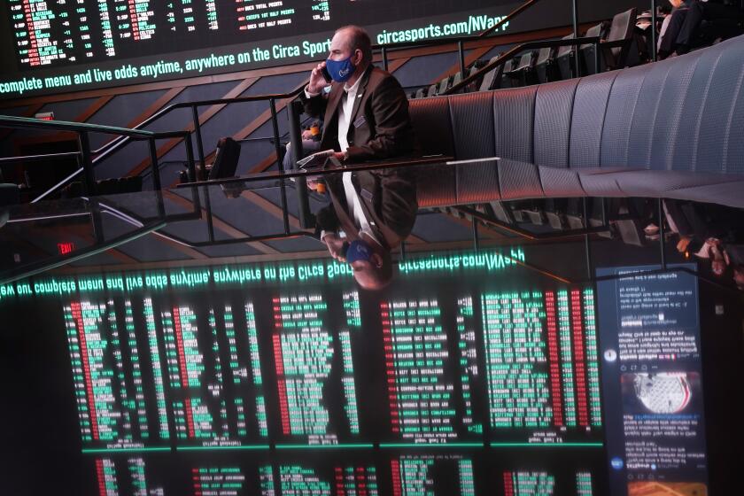 A man sits on a couch as betting odds for the Super Bowl are displayed on monitors at the Circa resort and casino sports book Wednesday, Feb. 3, 2021, in Las Vegas. (AP Photo/John Locher)