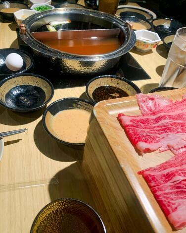 A metal divided pot with a wooden tray that holds raw meat, plus small dishes of sauce