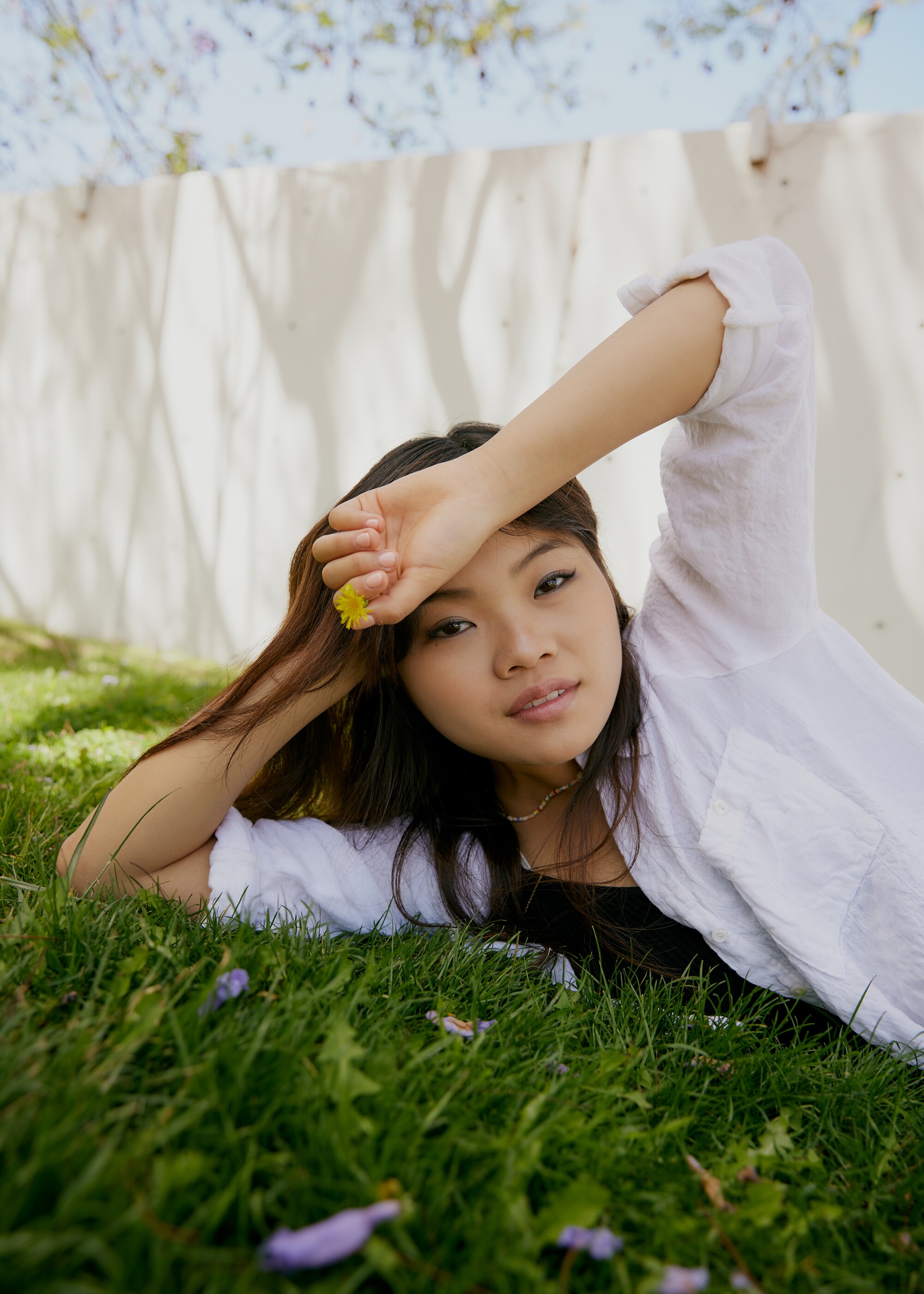 Miya Cech lays on the grass holding a small yellow flower.