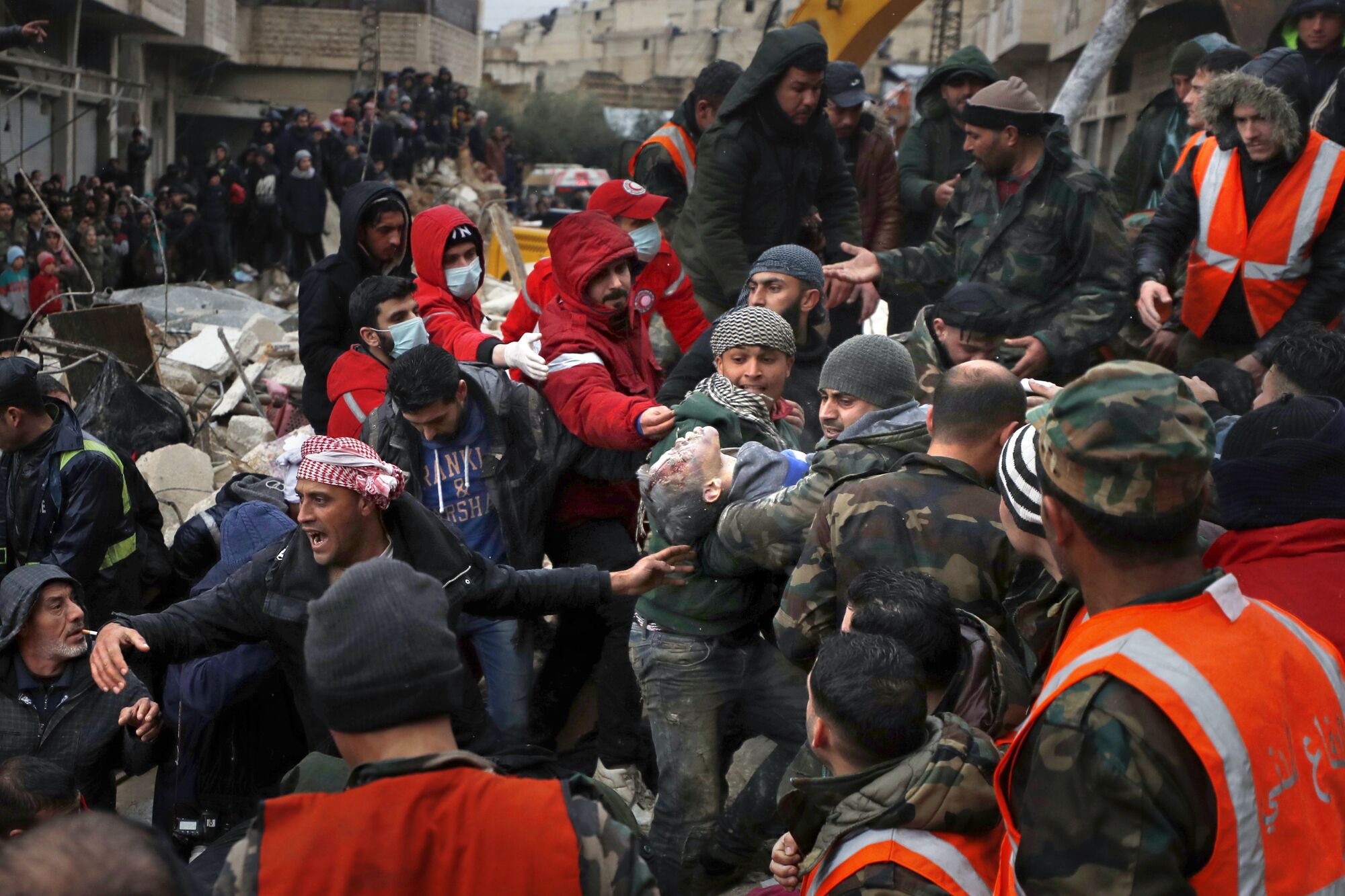 A large group of men and security forces help carry a young boy.