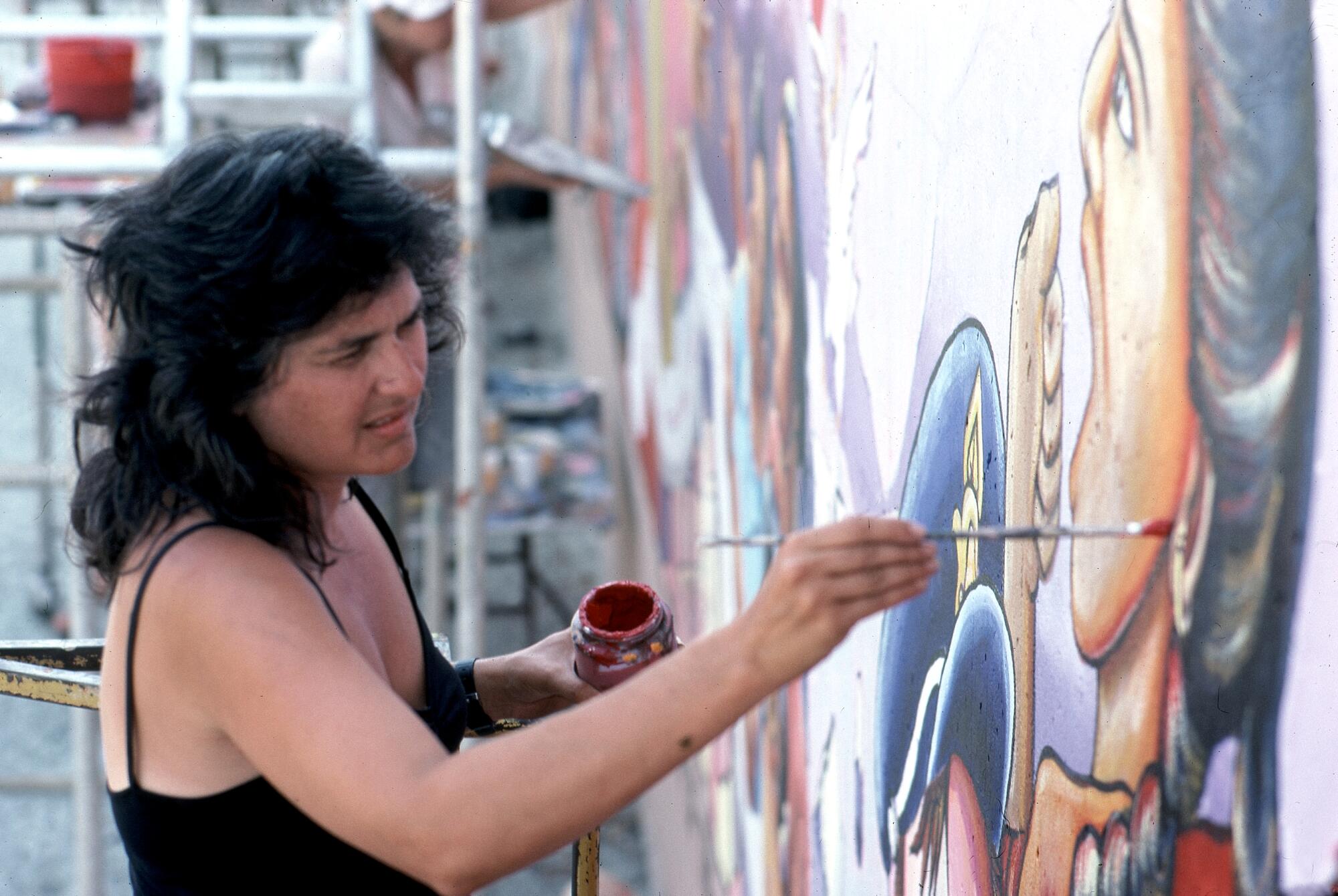 A woman paints on a wall with a thin brush.
