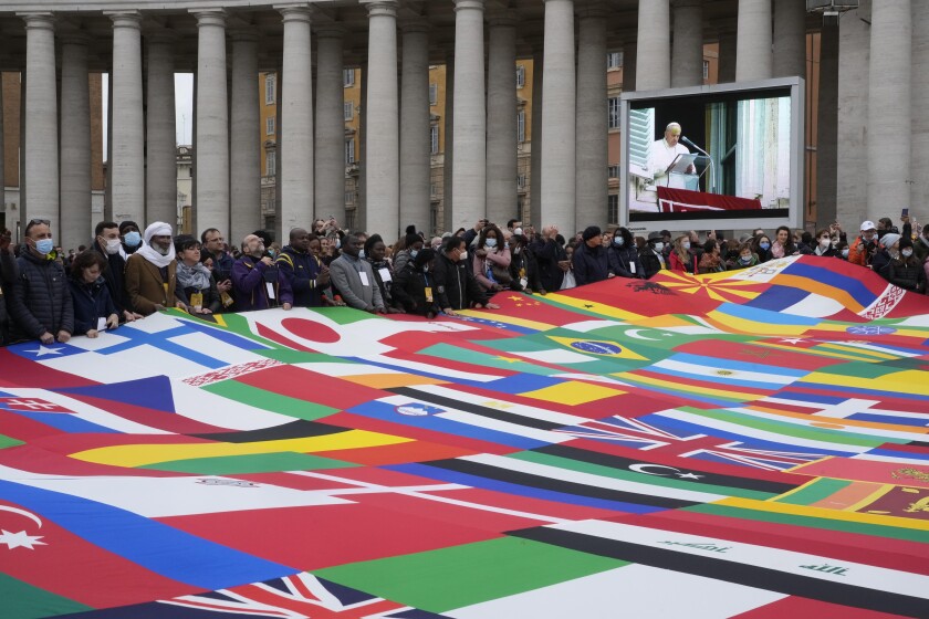 Miembros de una asociación de migrantes sostienen un letrero enorme hecho con varias banderas mientras el papa Francisco pronuncia la oración del Angelus en la Plaza de San Pedro, en el Vaticano, el domingo 28 de noviembre de 2021. (AP Foto/Gregorio Borgia)
