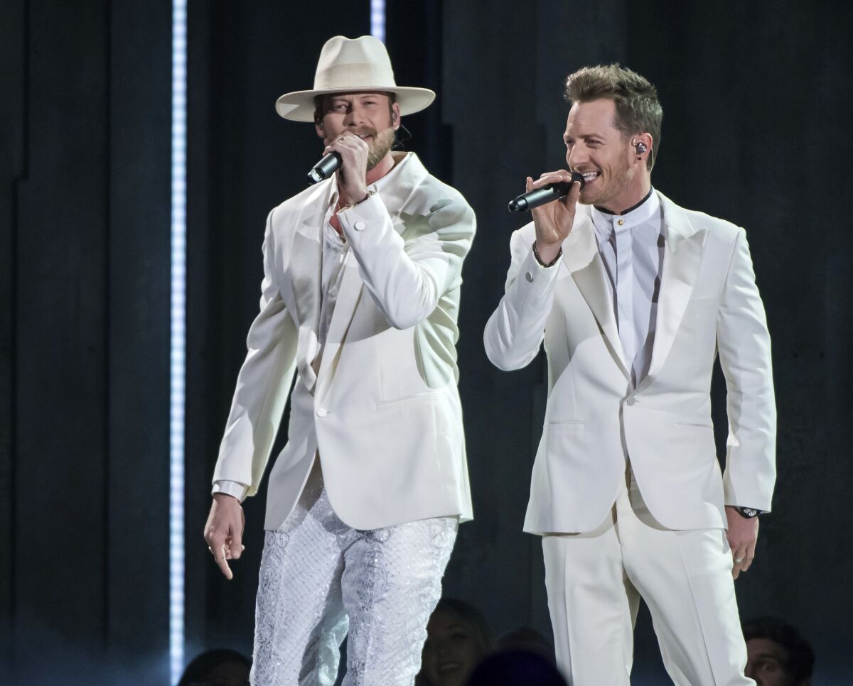 Two men in white suits sing into microphones.