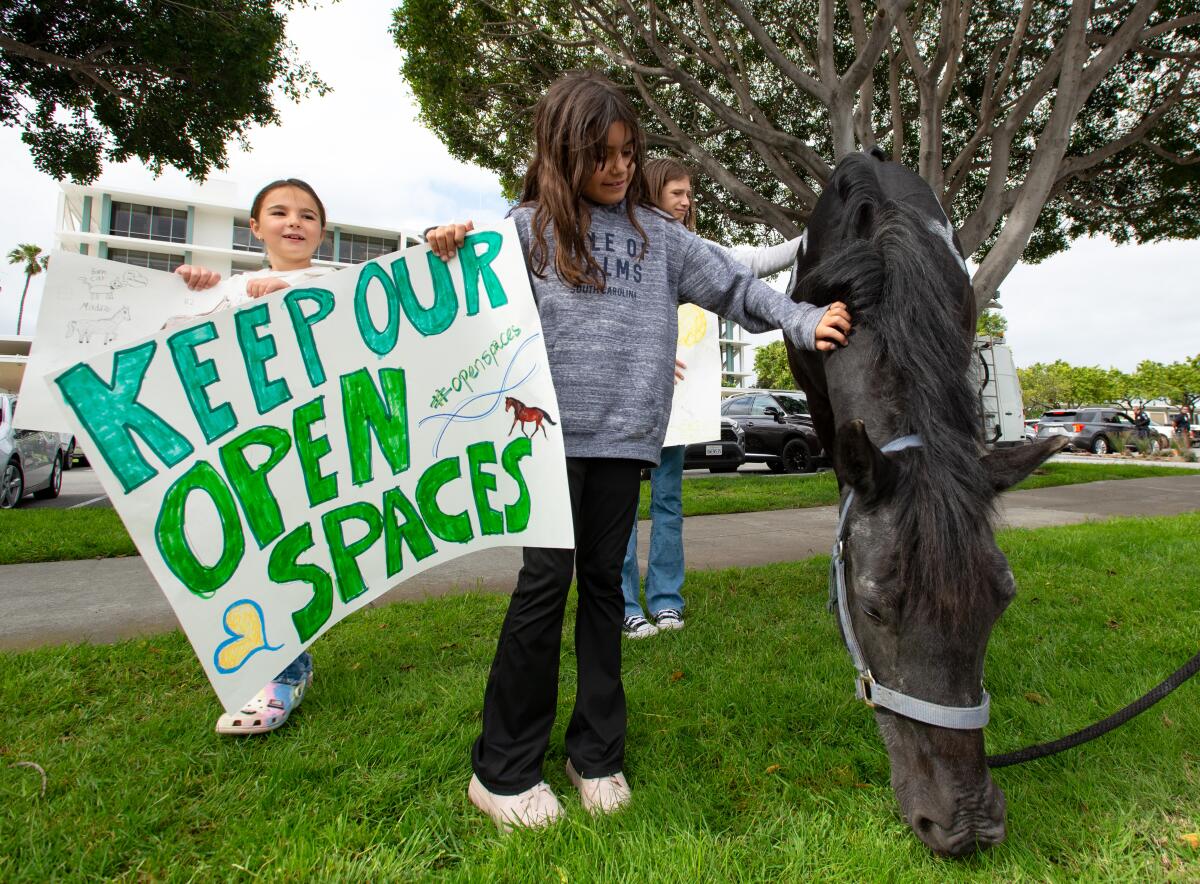Riding students pet Seren while holding signs against an increase in boarding fees.