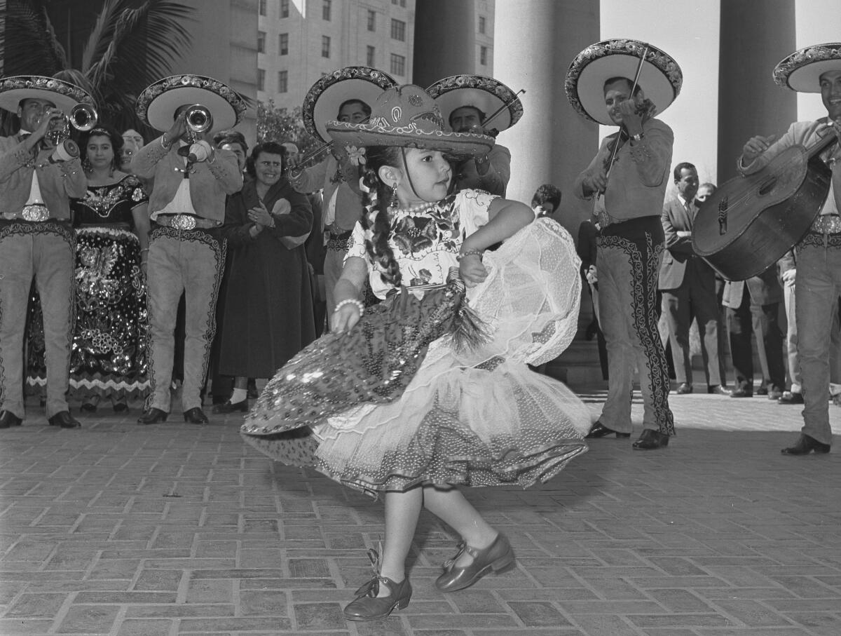 A girl dances in front of musicians playing horns. Everyone is in traditional costume.