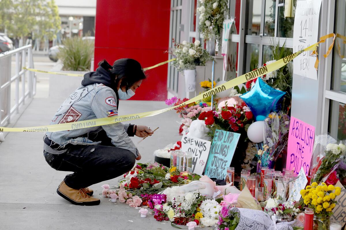 A kneeling man holds incense at a memorial at a Burlington store. Signs read "She was only 14" and "Abolish the police."