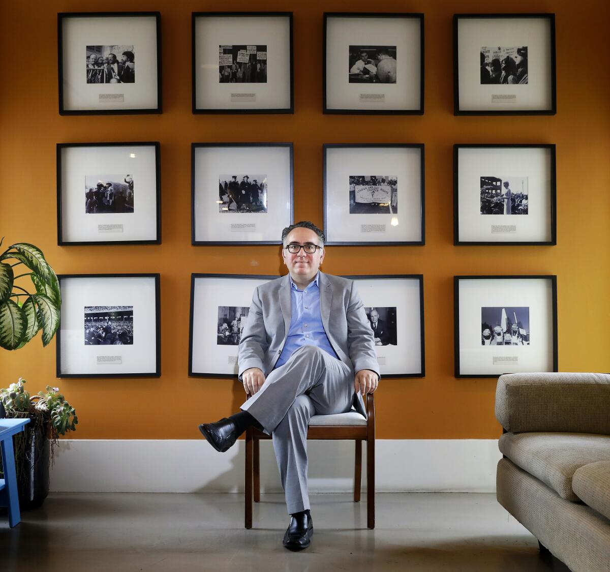 A person sits in a chair in front of a wall of framed photos.