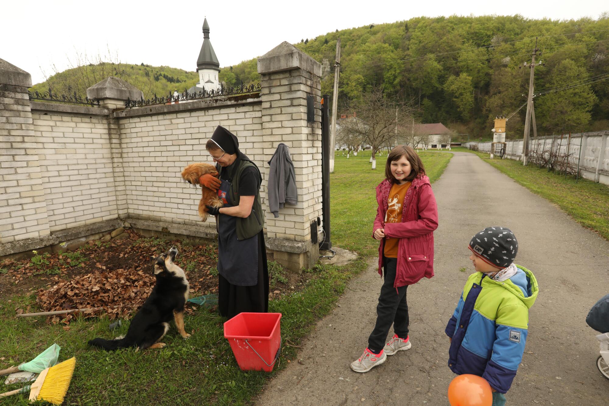 A nun holds a dog, standing beside two children 