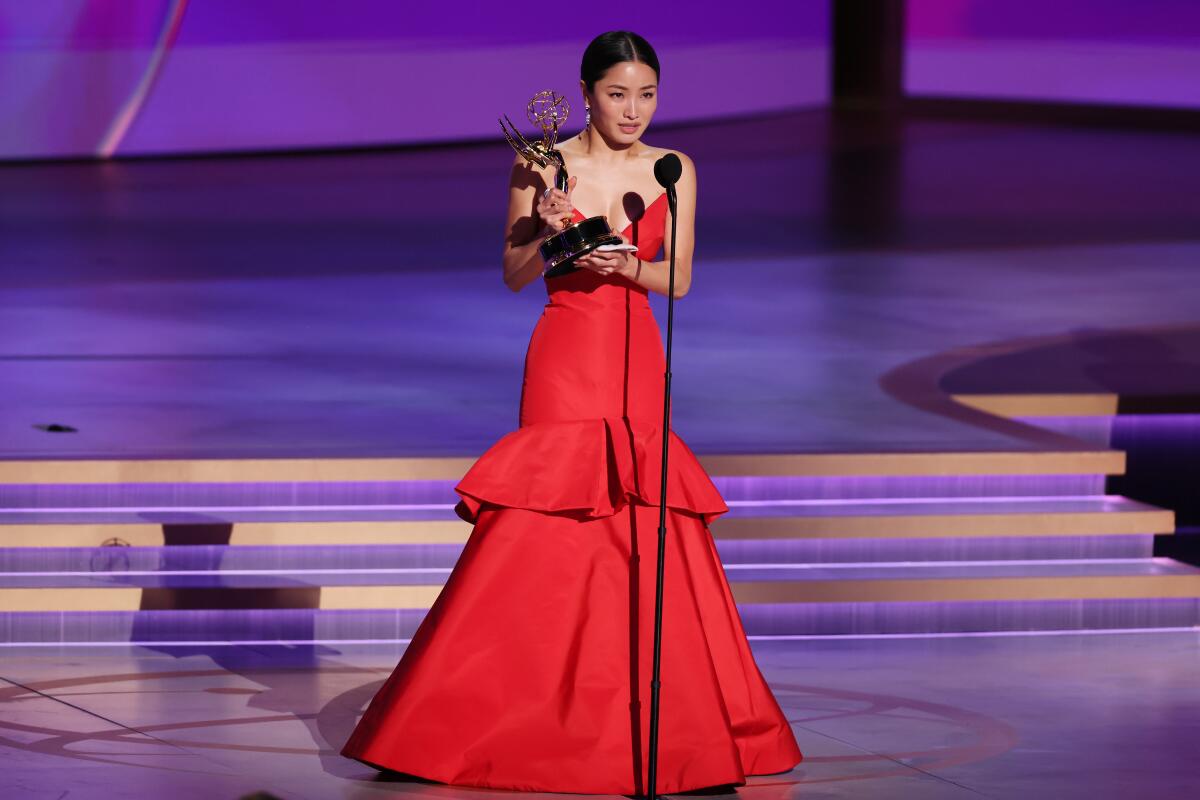 a woman in a red dress onstage holding an Emmy