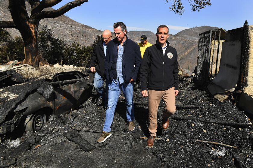 Wally Skalij  Los Angeles Times GOV. GAVIN NEWSOM, center, looks over the fire devastation in Brentwood with L.A. Mayor Eric Garcetti, right, and Councilman Mike Bonin, left rear. Newsom and the state face dual crises in blackouts and wildfires.