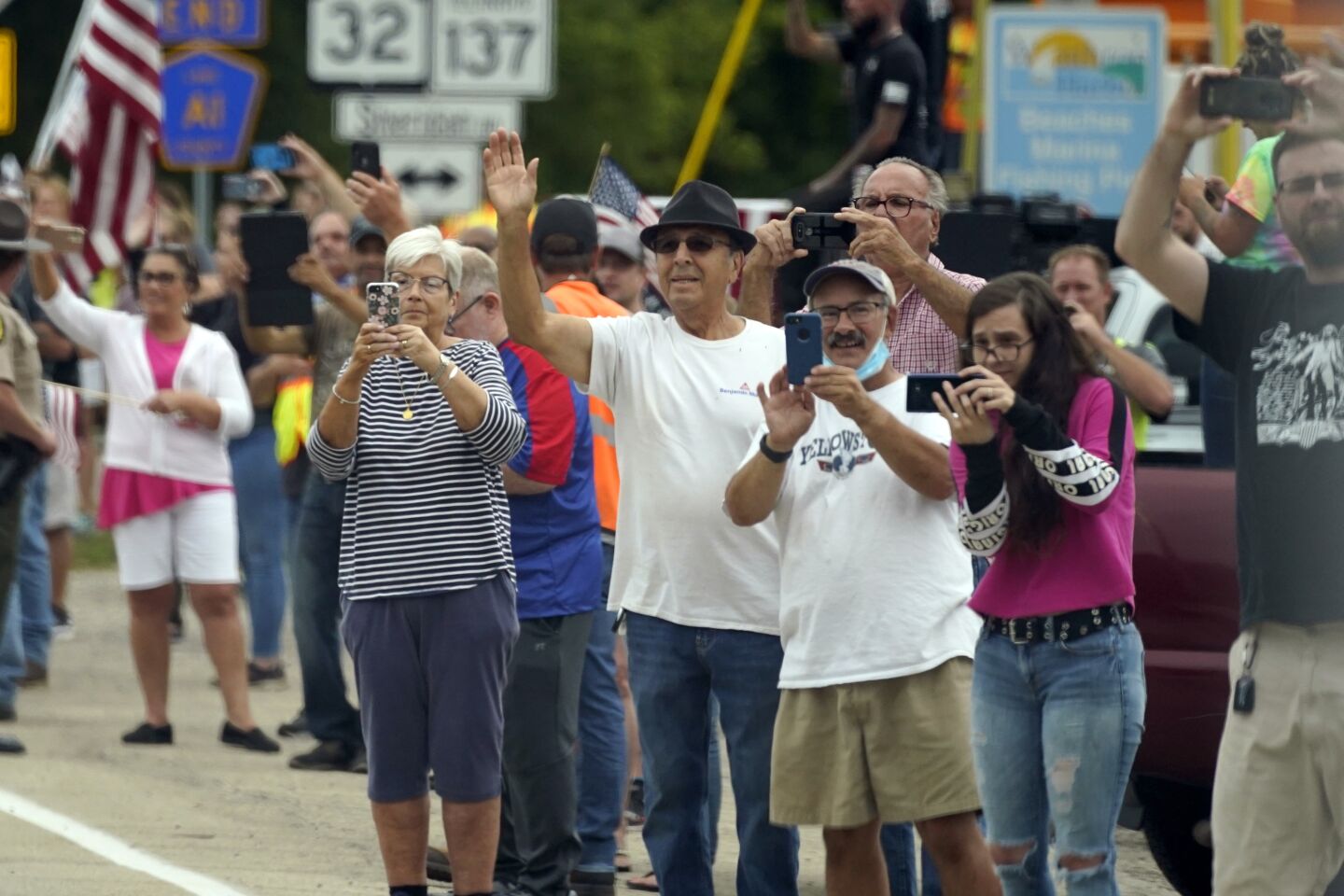 People without masks wave and take video and photos as President Trump's motorcade passes in Kenosha, Wis.