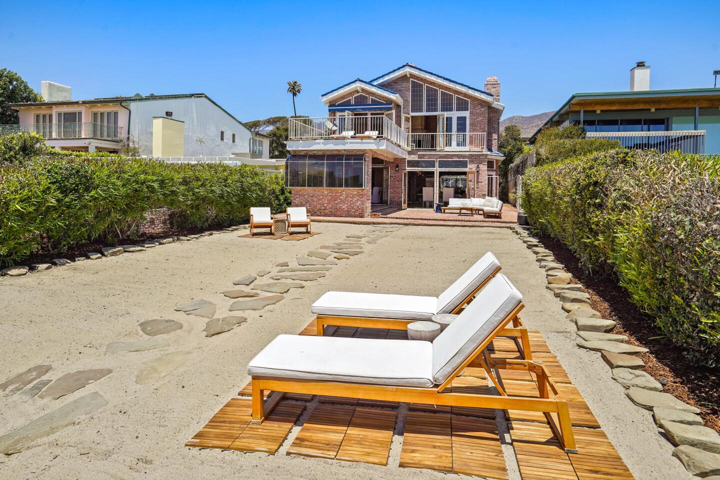 The oceanfront patio has deck chairs, a stone-covered walkway and a view of the house.