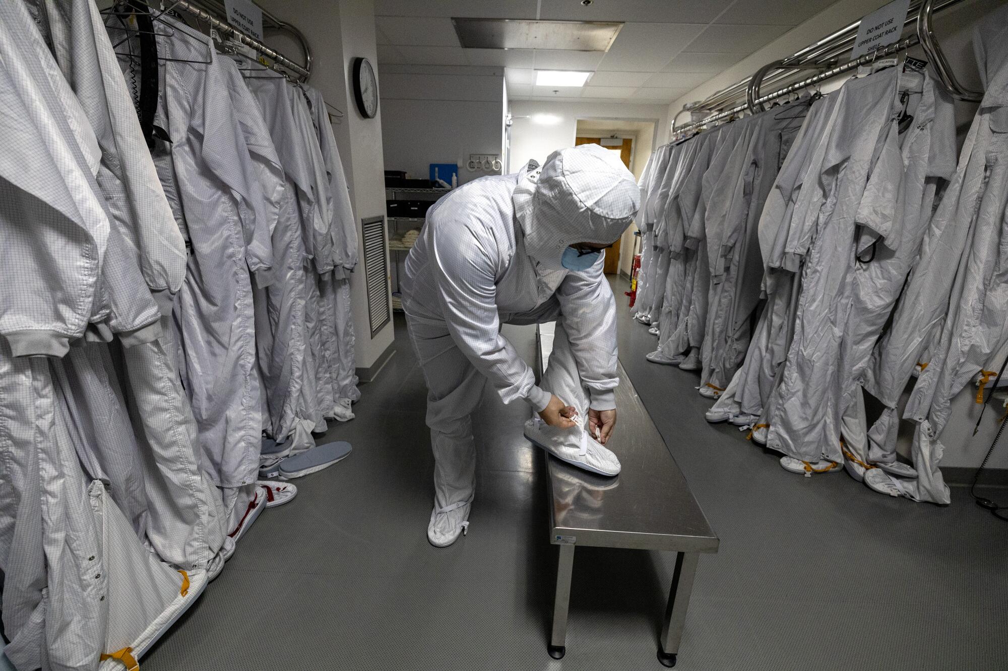 Mechanical engineer Steve Barajas leans over to close the leg of his clean room outfit