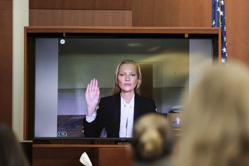 A woman in a black suit raising a hand on a screen in a courtroom