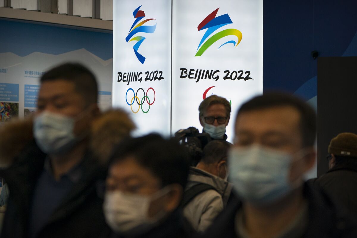 People wearing face masks look at an exhibit with their backs toward a Beijing 2022 sign.