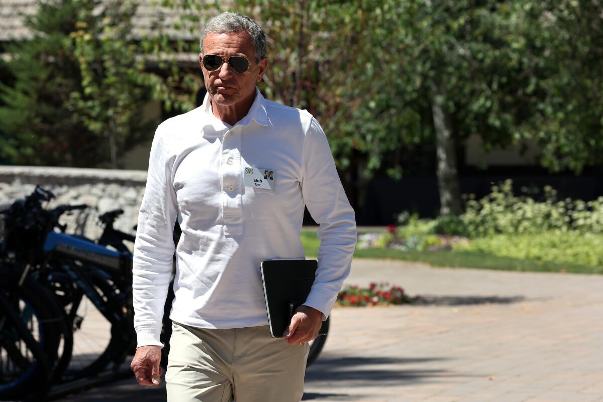 Disney's Bob Iger dons dark sunglasses, a white, long-sleeve button-down  shirt and khakis as he walks.