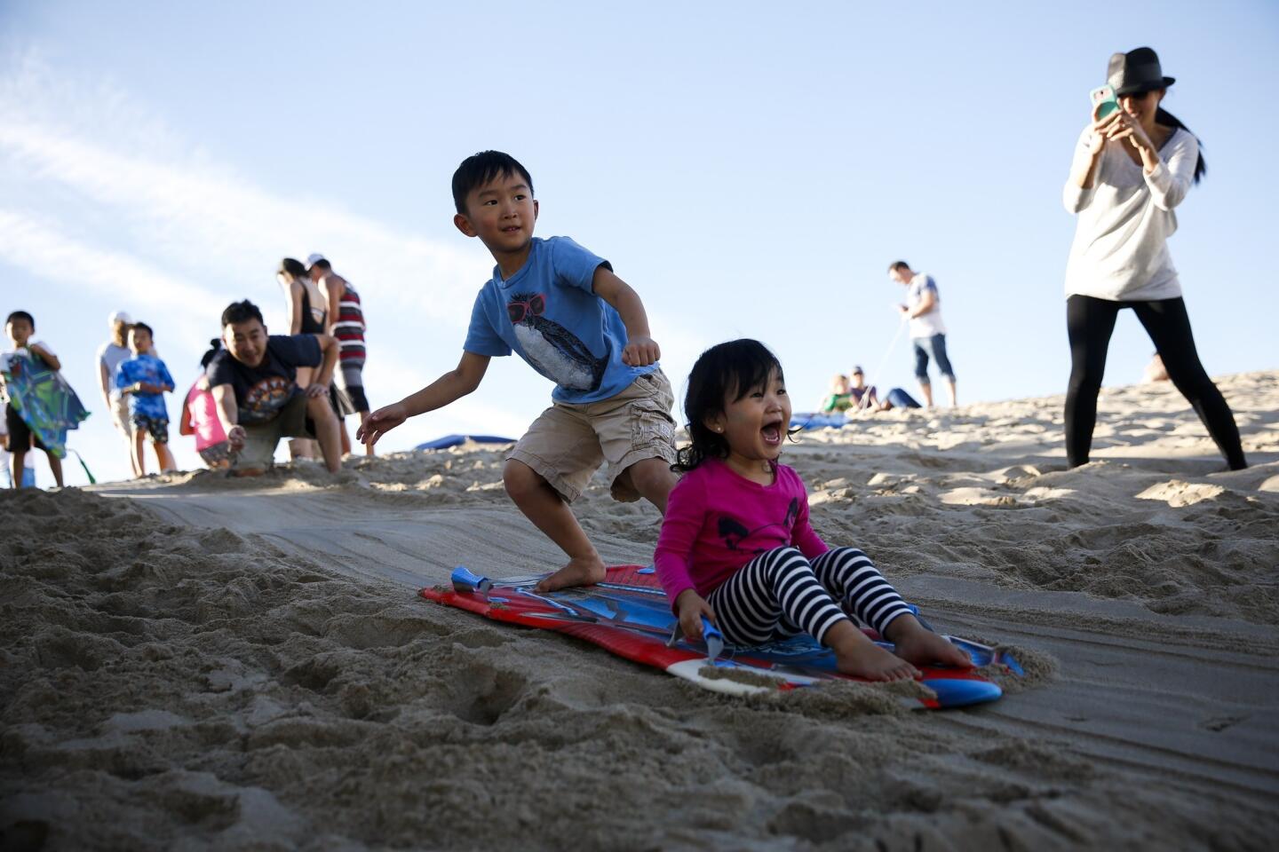 While their mom Jina takes pictures, Eden Inn, 2, of Redondo Beach lets out a scream, as brother Nathan, 5, rides their sled down a sand dune at the Hermosa Beach Pier on Christmas afternoon. The temperature reached the 80s in Hermosa Beach.