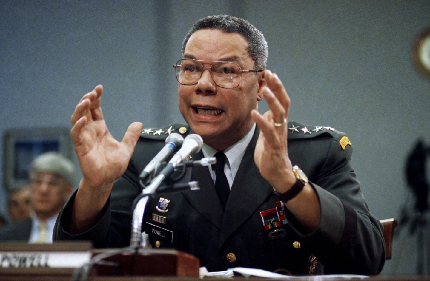 Gen. Colin Powell speaks in front of a microphone at a table on Capitol Hill in Washington