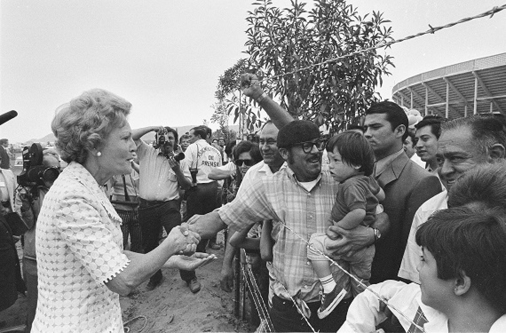 Mexican families reach across barbed wire to shake hands with Pat Nixon.