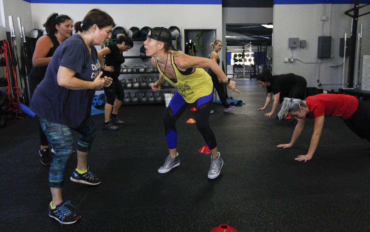 Fitness trainer Lacey Stone, center, motivates student Carrie Carr, left, as she does an exercise called foot fire to improve foot speed and quickness during a two-week boot camp class.