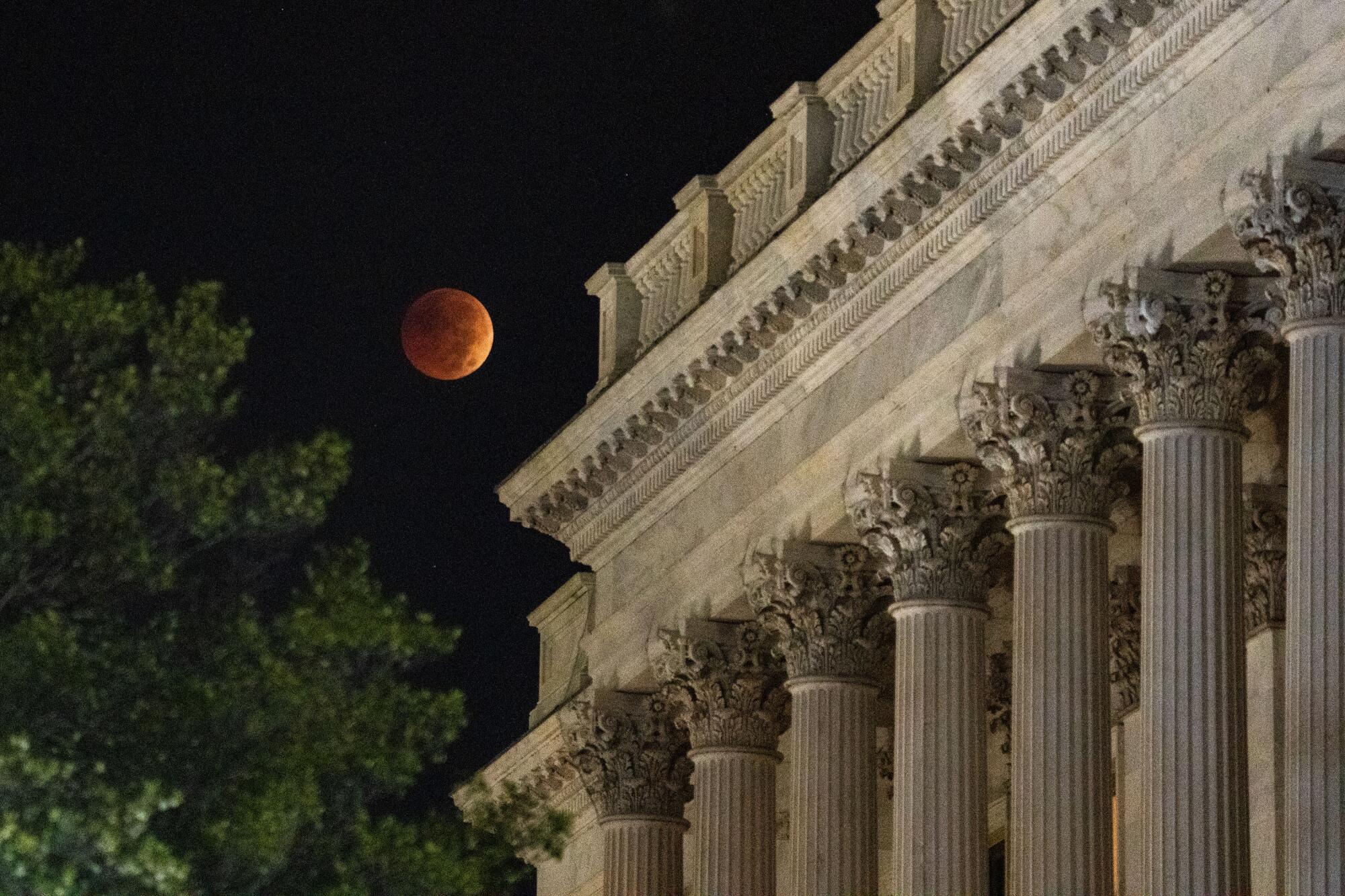 A blood moon lunar eclipse appears to hover beyond the U.S. Capitol Building in Washington, D.C.
