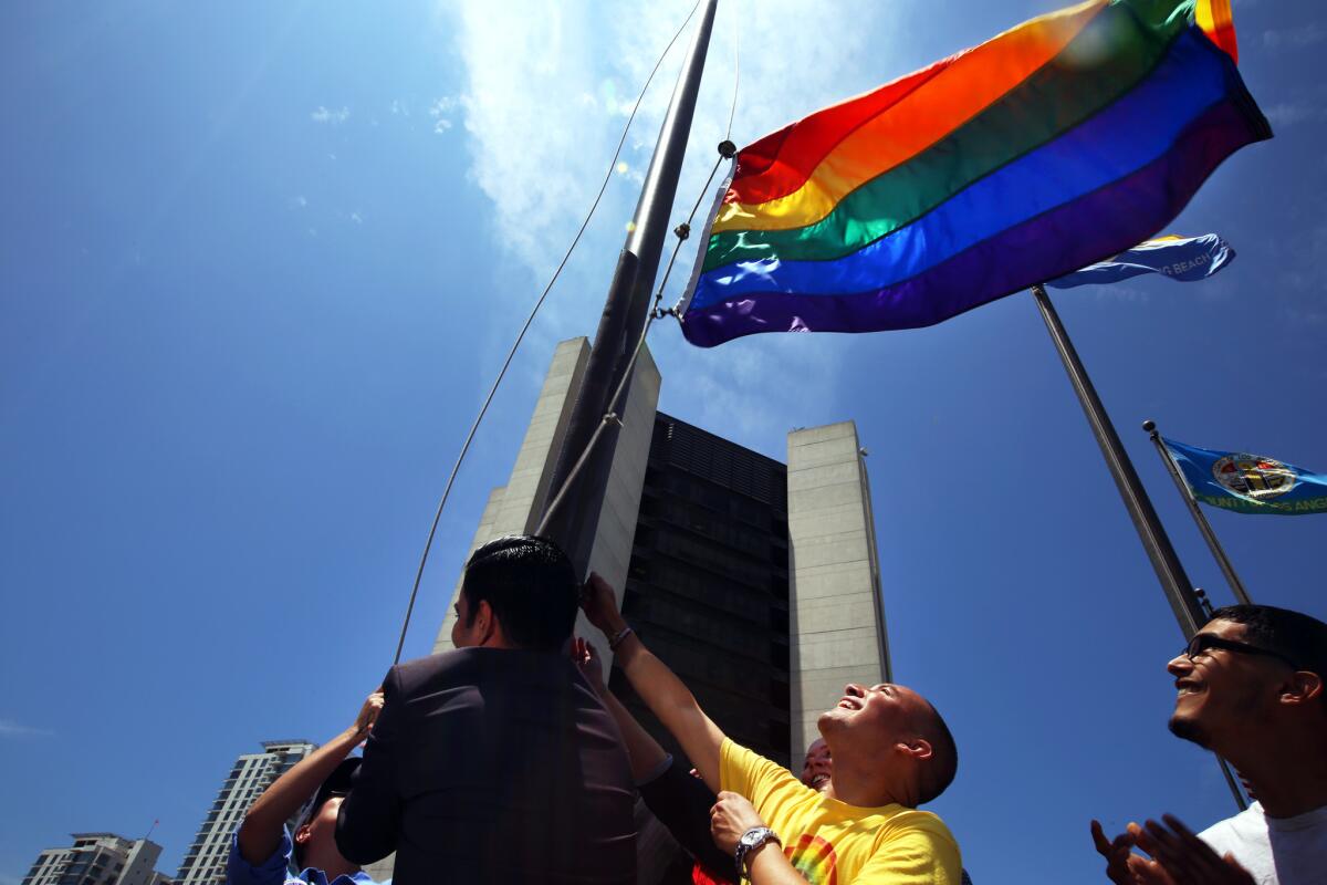 Long Beach Mayor Robert Garcia, with his back to the camera, the city's first openly gay mayor, and Mark Magdaleno, 43, of Long Beach, right, raise a gay pride flag over the Civic Plaza in response to the Supreme Court ruling.