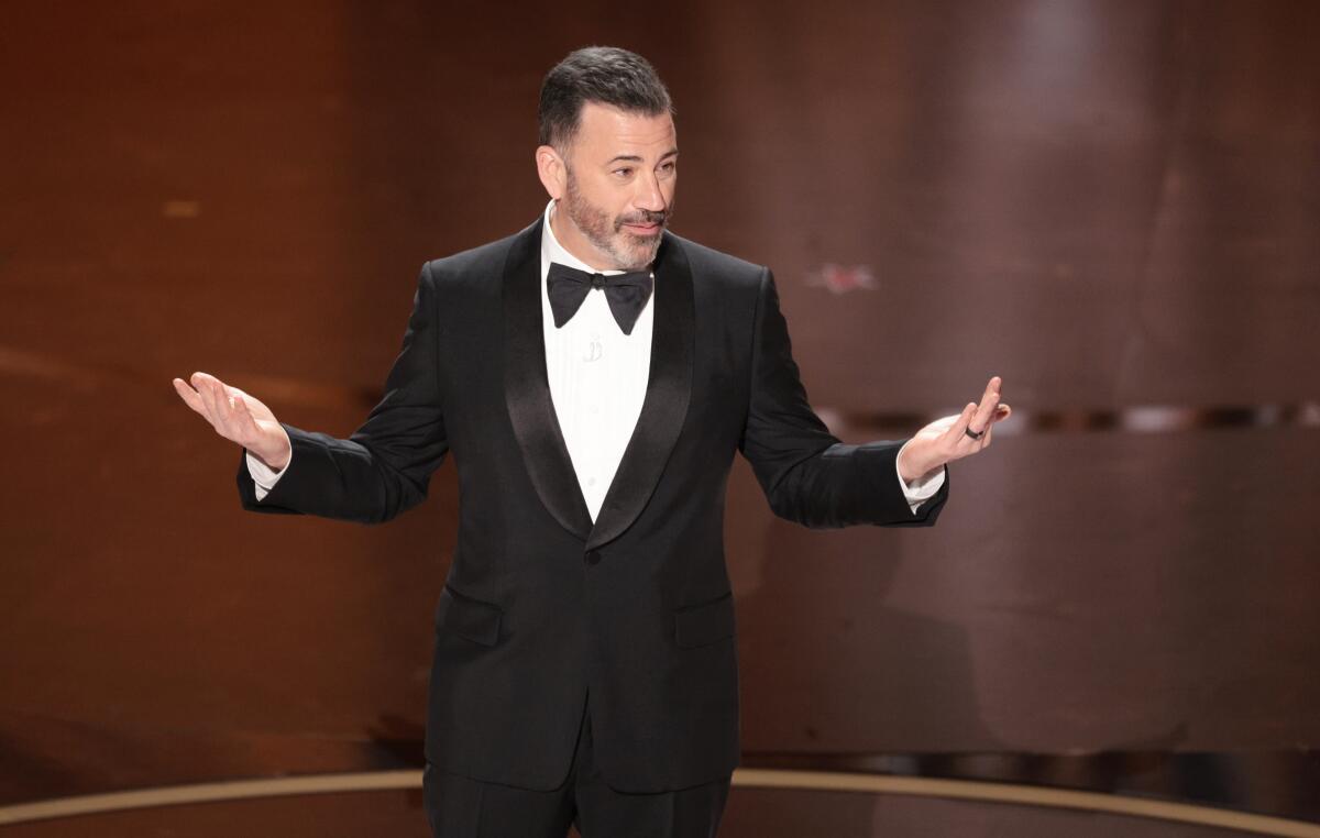 Jimmy Kimmel in a tuxedo with a bowtie, standing onstage gesturing with his hands out to his sides 