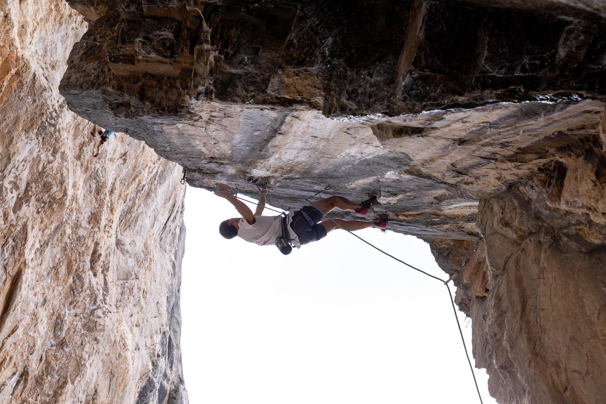 A climber hangs high oiff the ground from a horizontal shelf of rock.