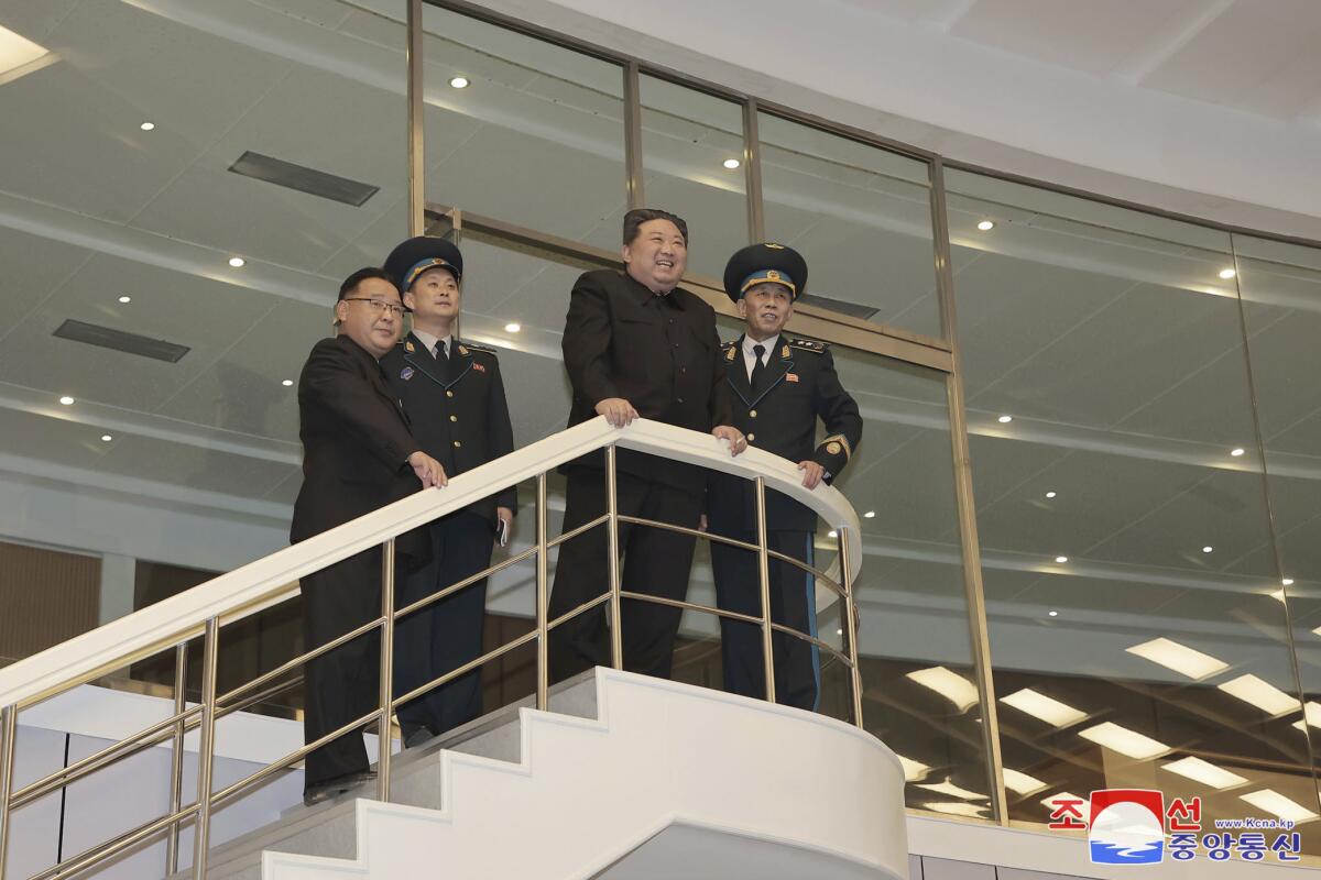Kim Jong Un and three other men stand atop a staircase looking out 