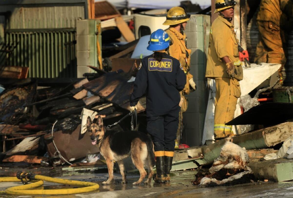 Karina Peck guides a dog trained in detecting human remains through the rubble of a fatal fire at a Compton auto mechanic's shop.