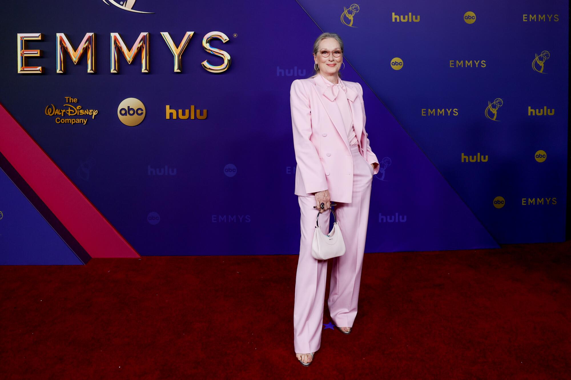 Meryl Streep wears a pink suit with a long bow. 