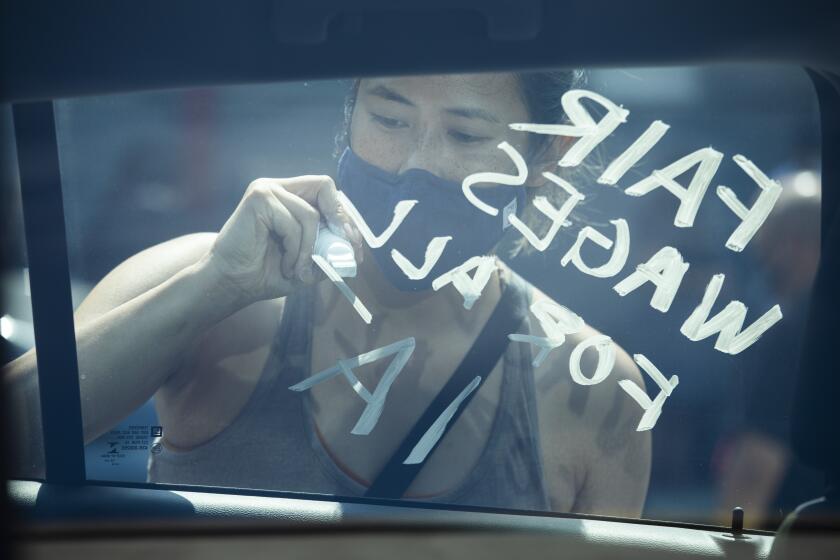 LOS ANGELES, CA - SEPTEMBER 26: Donna Young of IATSE Local 700 Motion Picture Editors Guild, writes a message of "fair wages for all" on a union member's car during a rally at the Motion Picture Editors Guild IATSE Local 700 on Sunday, Sept. 26, 2021 in Los Angeles, CA. Up to 60,000 members of the International Alliance of Theatrical Stage Employees (IATSE) might go on strike in the coming weeks over issues of long working hours, unsafe conditions, less pay from streaming companies and demand for better benefits. (Myung J. Chun / Los Angeles Times)