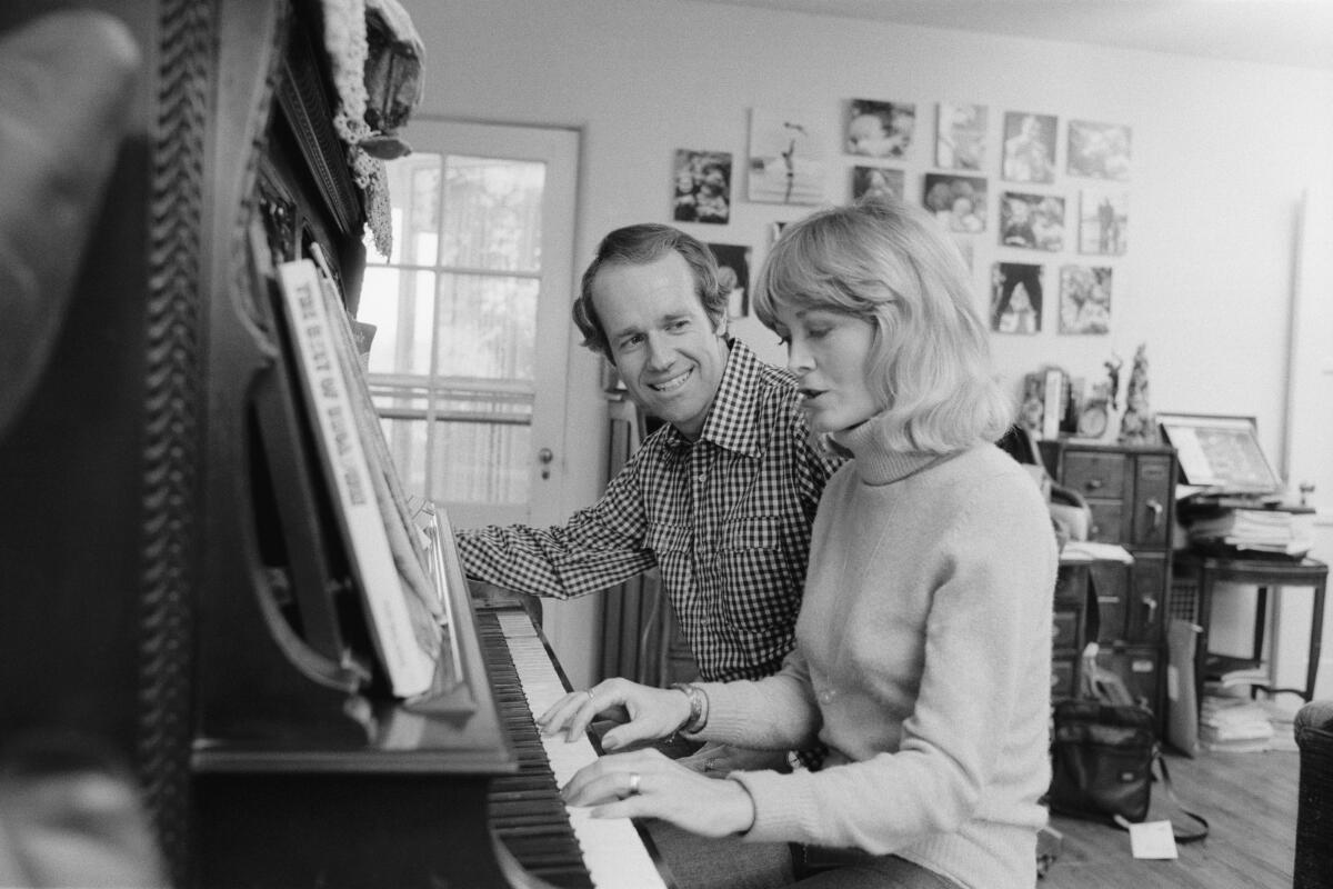 A man and a woman seated at a piano, with the woman playing it.