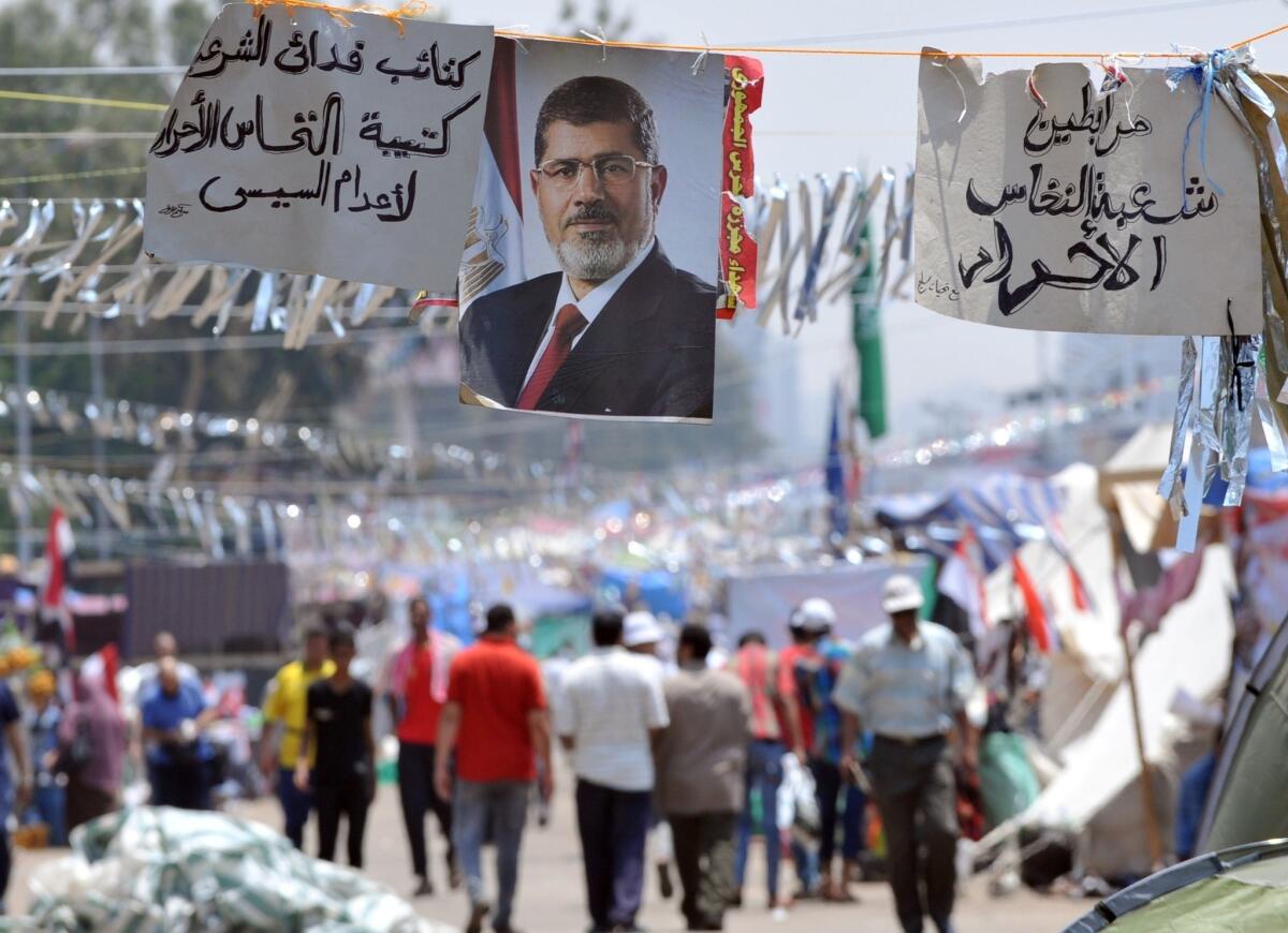 Supporters of Egypt's deposed President Mohamed Morsi walk past his portrait in Cairo on Tuesday during a sit-in outside Rabaa Al Adawiya mosque.