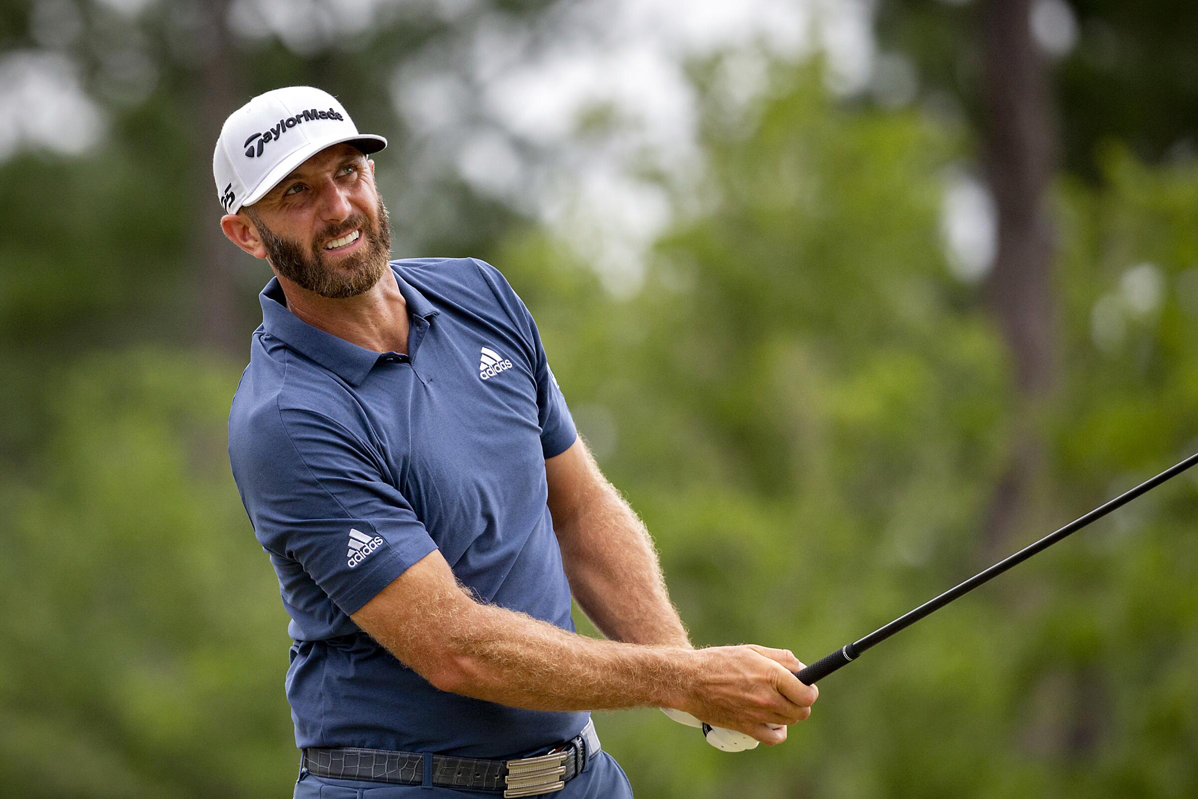 Dustin Johnson watches his drive while holding his gold club.