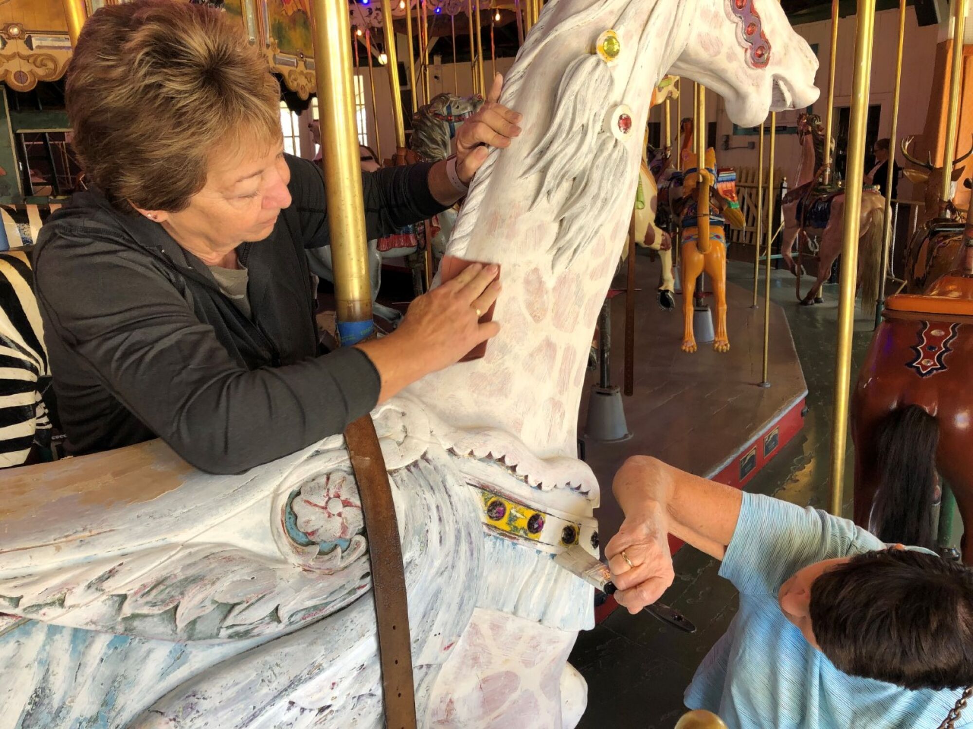 Volunteers Tracey Ferguson and Gloria Shepard sand and prime a carousel giraffe.