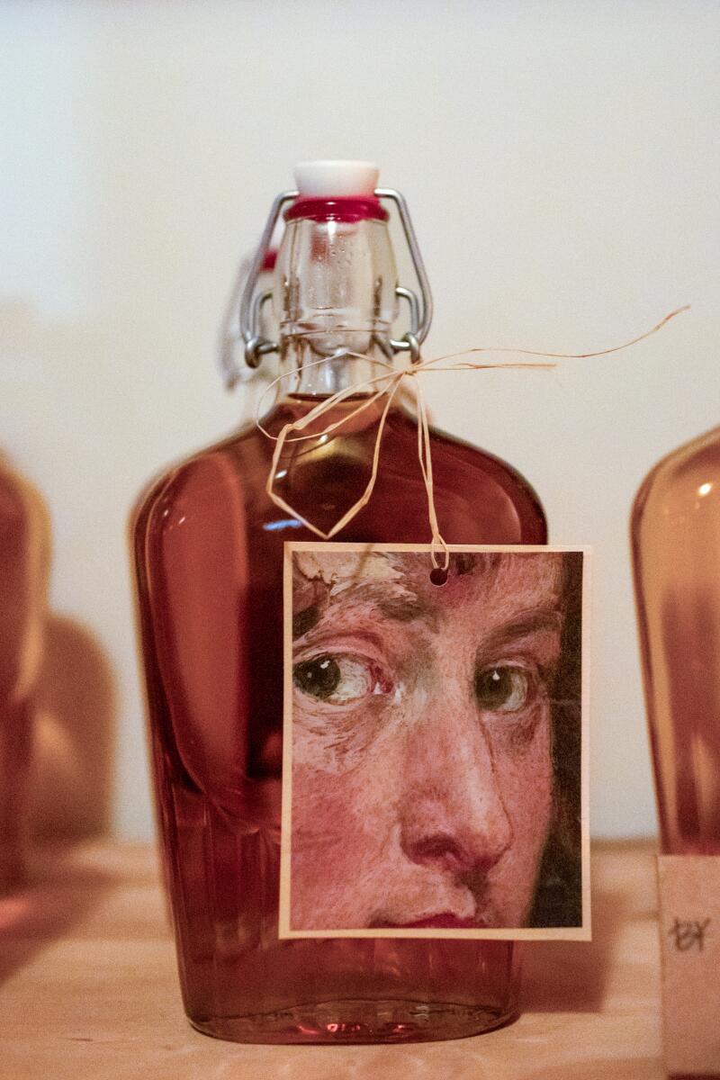 A liquid-filled bottle adorned with a tag with a painted closeup portrait of a person's face