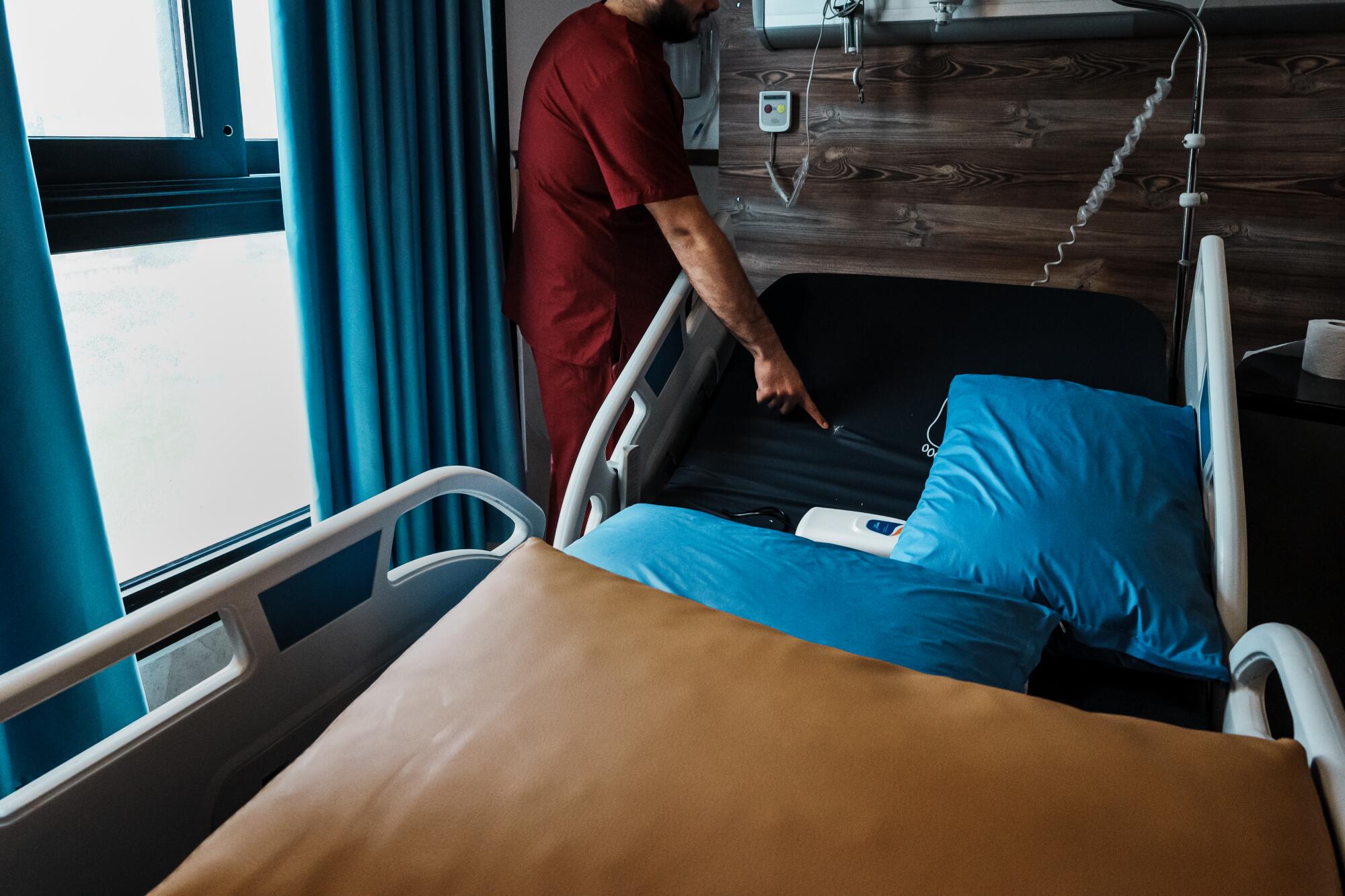A hospital worker in a red uniform points to a hole on a hospital bed with blue pillows