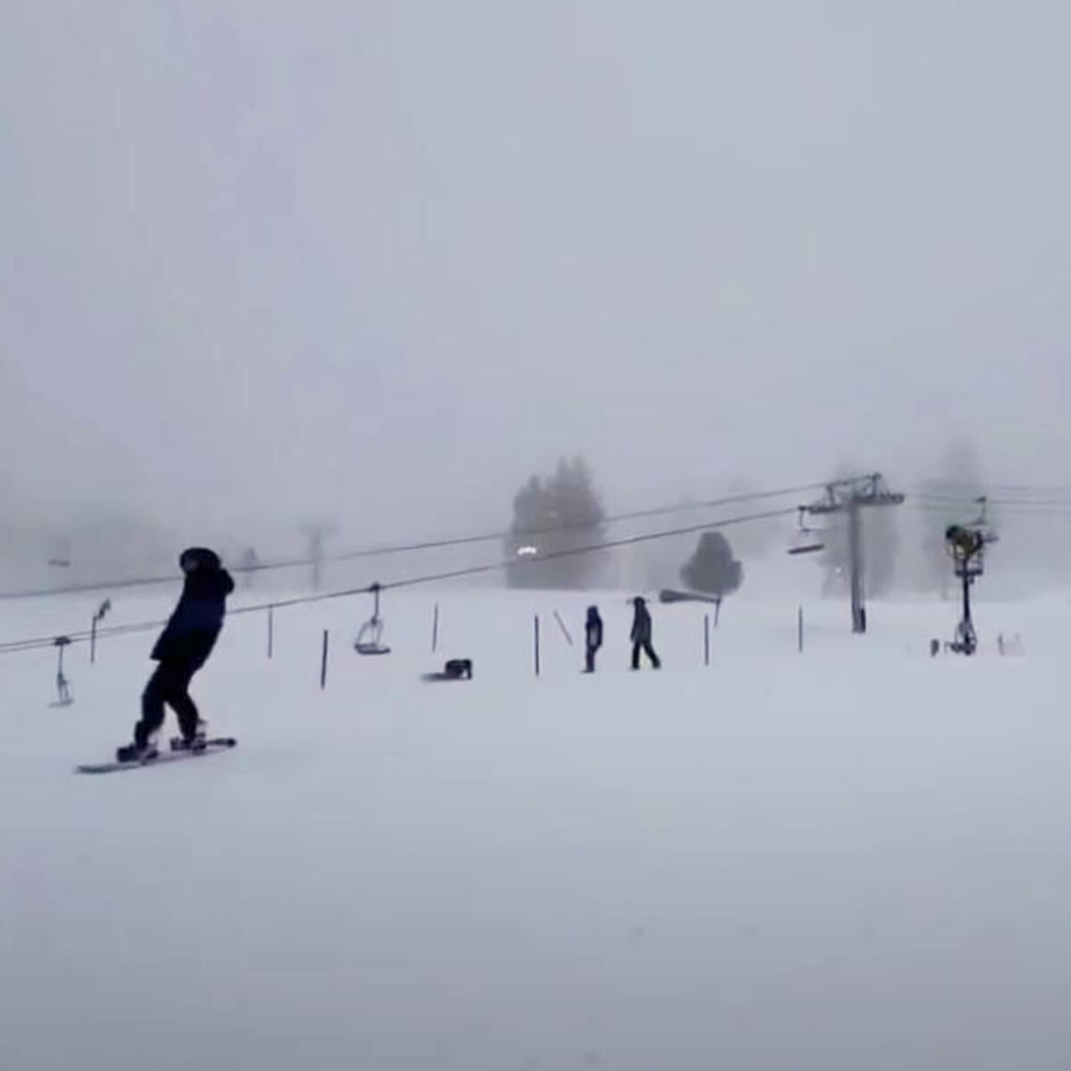 A person snowboards; two others stand beneath a ski lift.