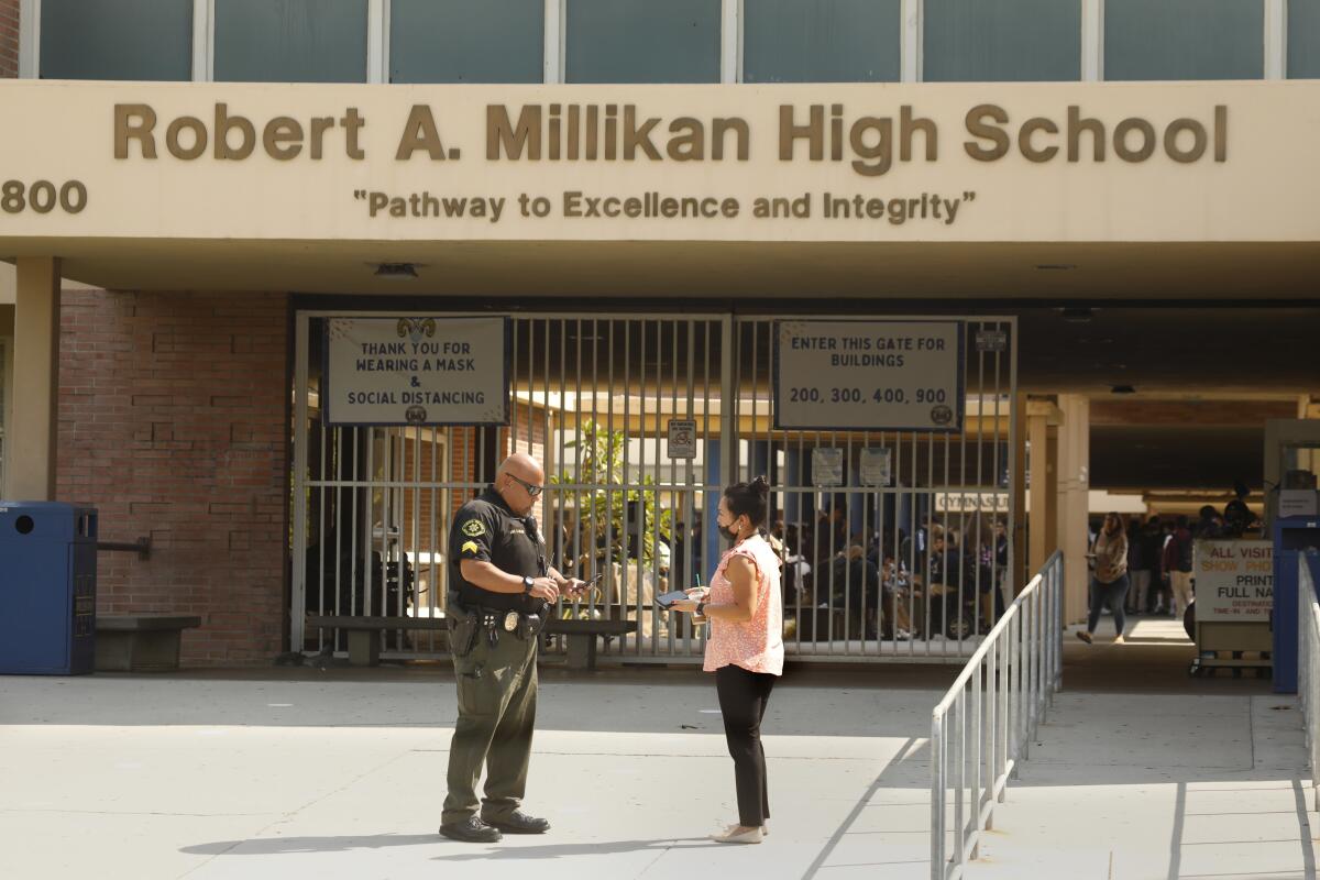 A Long Beach Unified School District police officer speaks to a woman outside Robert A. Millikan High School on Wednesday.