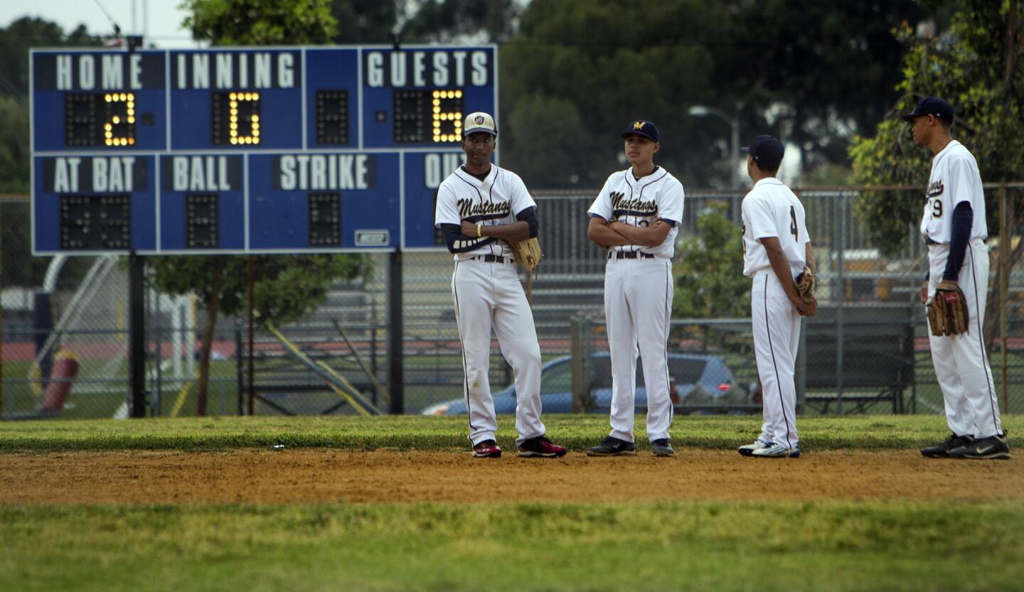 Muir players gather during a pitching change on April 24. The tattered field conditions include clumps of dying grass in the infield, chunks of dirt in a rutted right field and a sloping hill toward a muddy basin in left field.