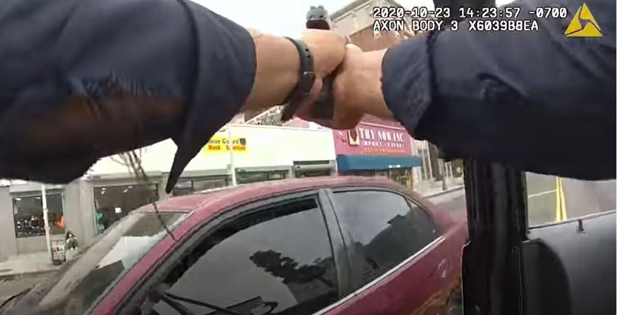An image from body camera video shows a police officer's hands clasping a gun.