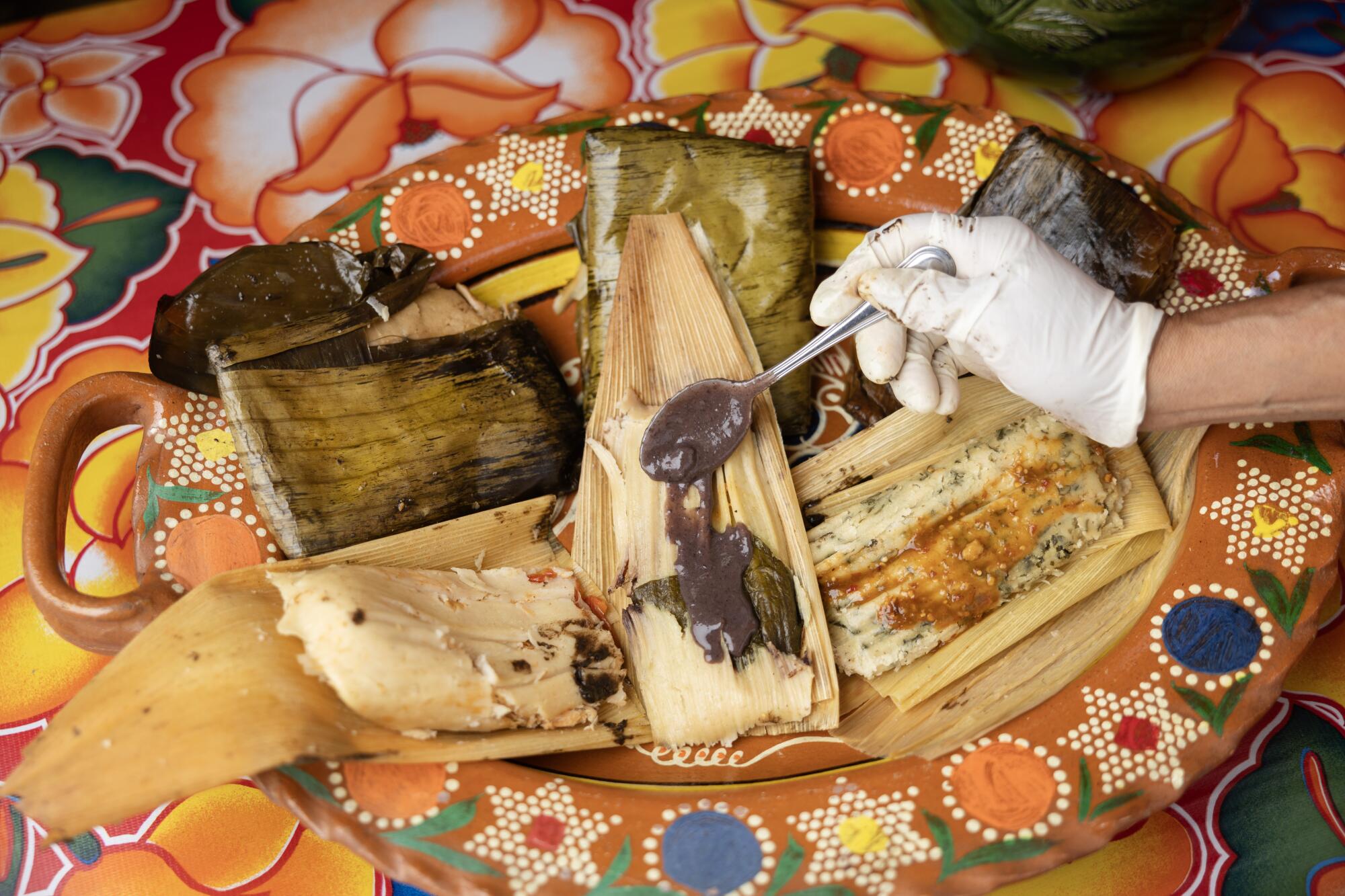 A plate of tamales gets a spoonful of sauce at Sabores Oaxaqueños Restaurant in Koreatown.